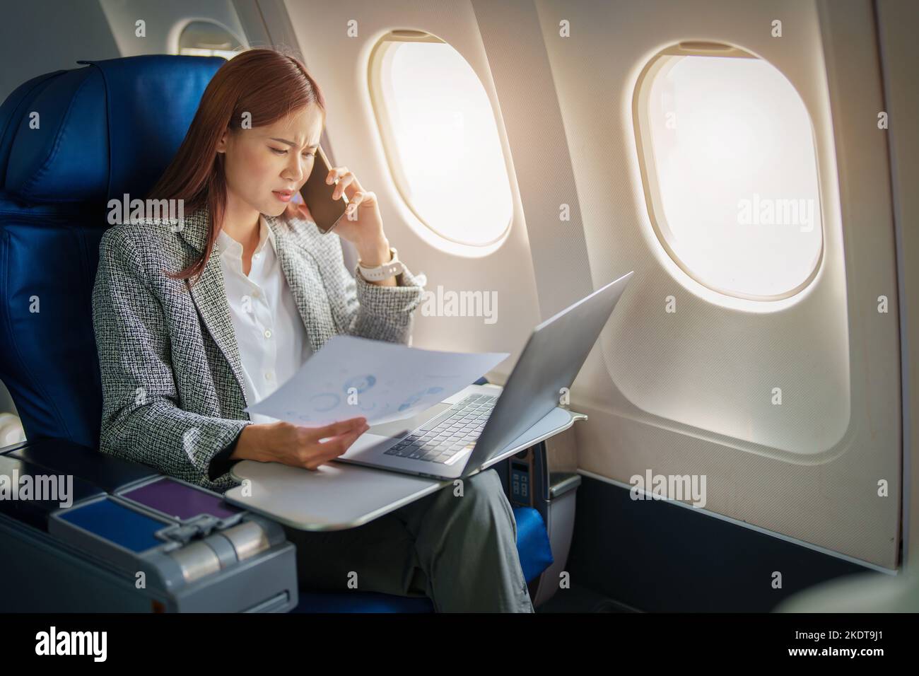 Portrait d'une femme d'affaires ou d'un entrepreneur asiatique couronné de succès dans un costume formel sur un avion assis en classe affaires à l'aide d'un téléphone, ordinateur portable Banque D'Images