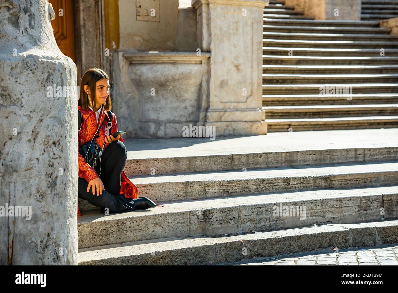 Jeune femme adulte assise seule sur les marches espagnoles à Rome, en Italie, portant un dessus rouge et des bottes de cow-boy Banque D'Images