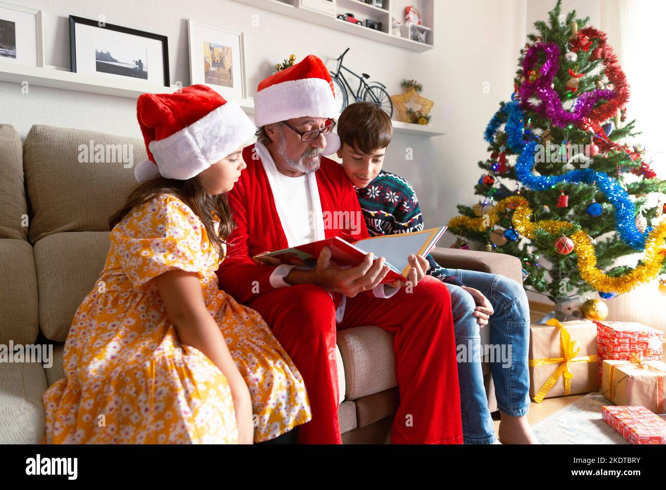Grand-père habillé comme le Père Noël lisant une histoire à ses petits-enfants à la maison. Noël, vacances. Banque D'Images
