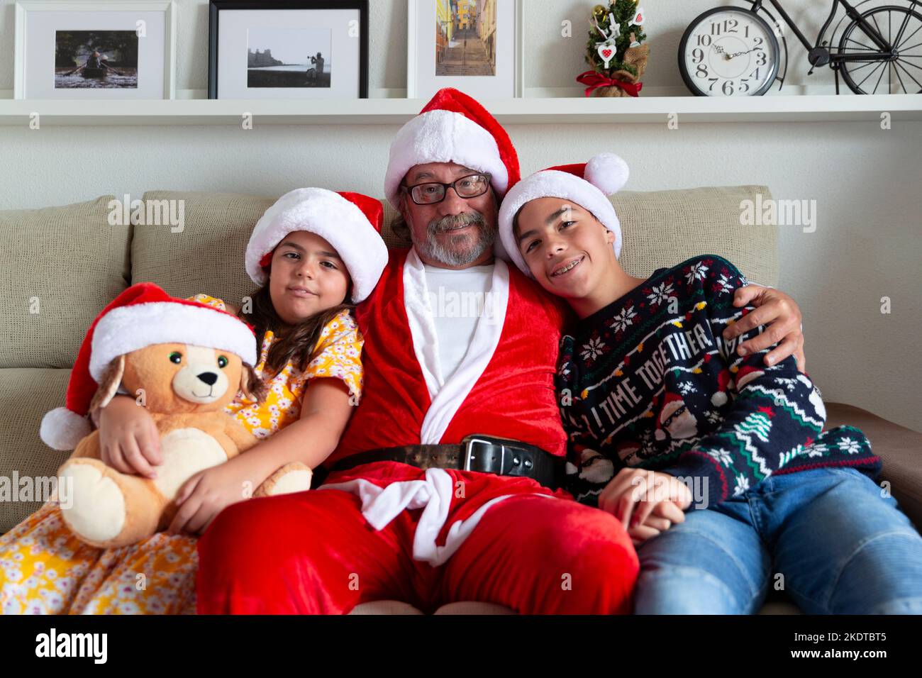 Noël à la maison. Portrait de famille du grand-père habillé comme le Père Noël embrassant ses petits-enfants. Banque D'Images