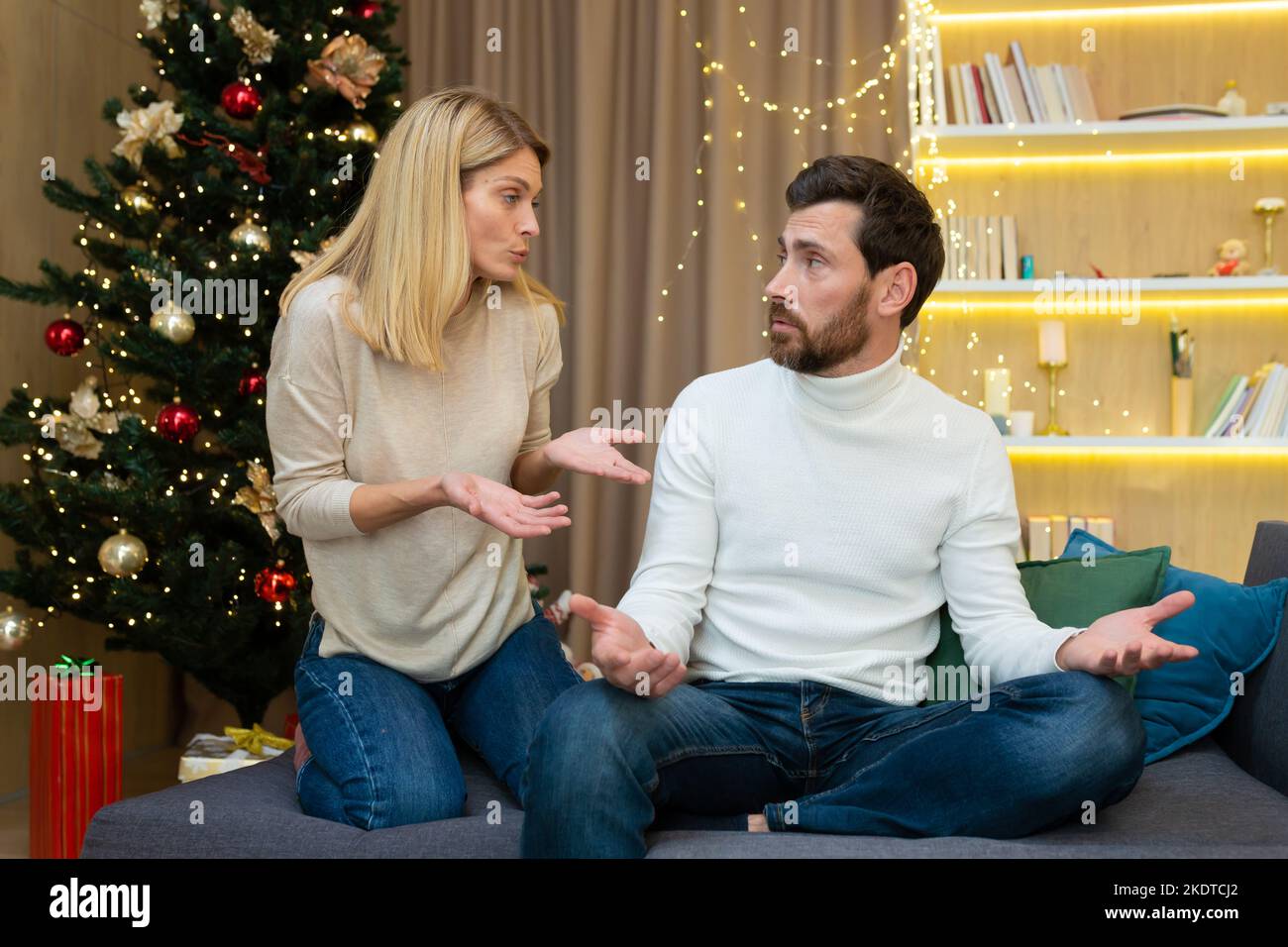 Conflit familial pendant les vacances. Un jeune couple, une famille, un homme et une femme se disputent à Noël. Ils sont assis sur le canapé à la maison près de l'arbre de Noël, criant l'un à l'autre. Banque D'Images