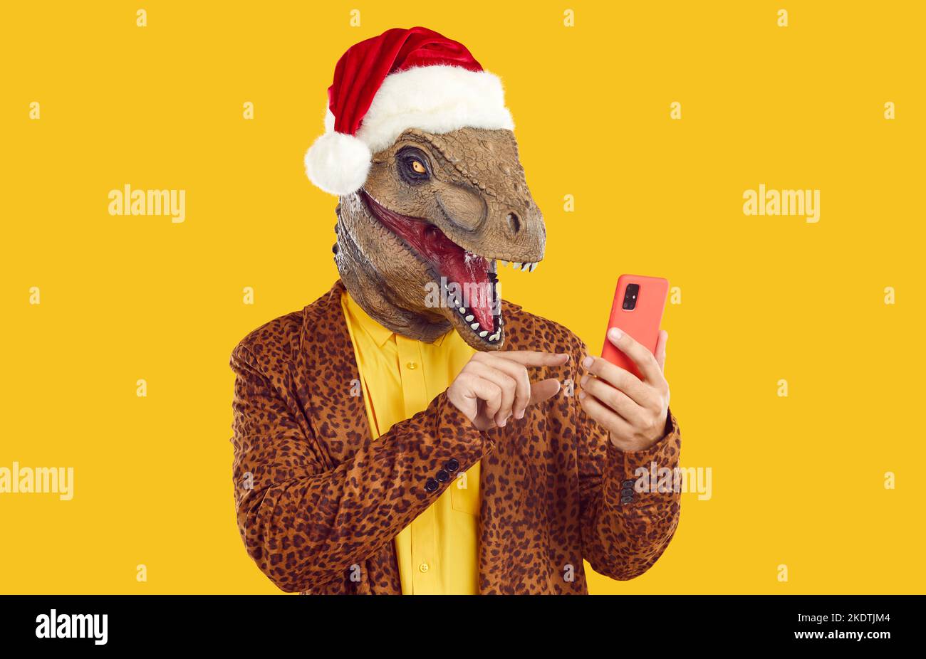 Homme drôle portant un masque de dinosaure, un chapeau de Noël et un costume de léopard en utilisant un téléphone portable Banque D'Images