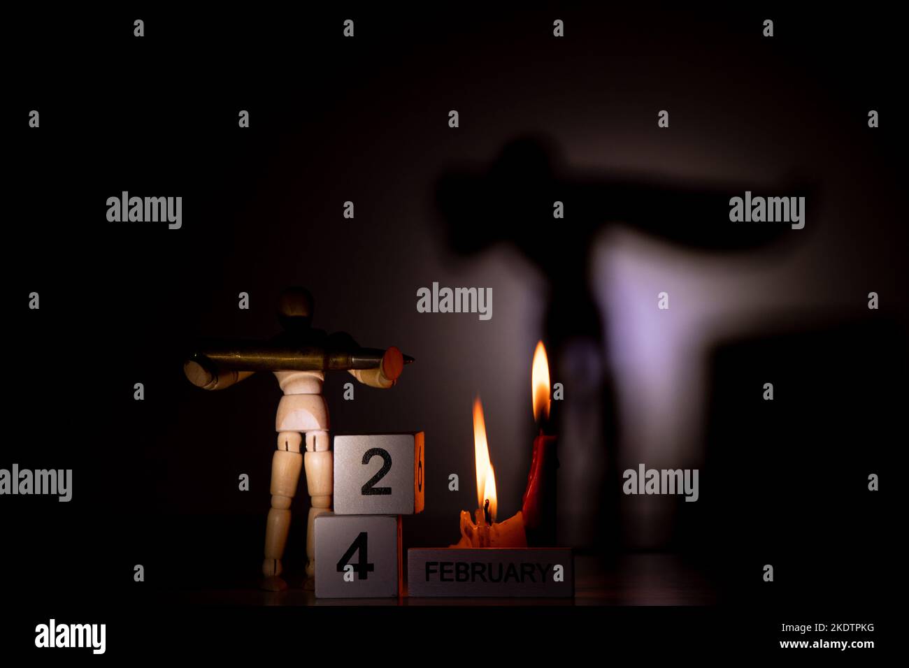Calendrier en bois avec la date 24 février, le premier jour de la guerre en Ukraine et un homme en bois tenant une balle dans l'obscurité près d'une flamme de bougie, Hist Banque D'Images