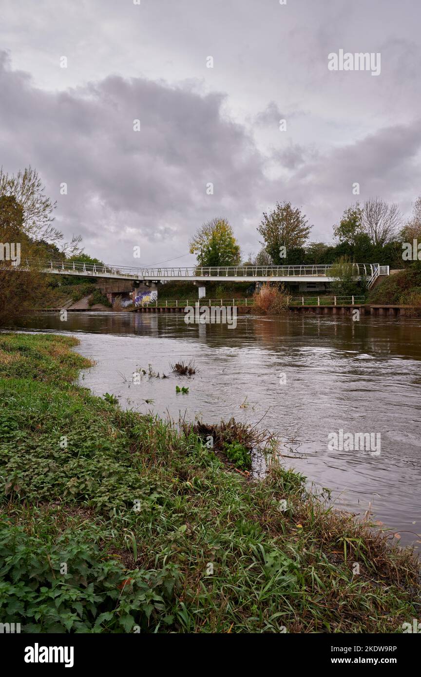 07 Nov 2022 - Hereford UK: Passerelle avec graffiti sur rivière gonflée sous ciel nuageux depuis la rive Banque D'Images