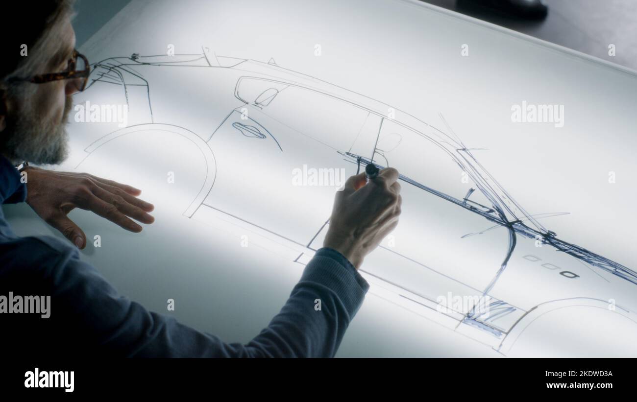 Un homme de conception automobile senior dessinant un plan avec un marqueur à la table lumineuse, développant un design futuriste de voiture électrique. Il travaille dans un studio de développement de conception automobile moderne. Banque D'Images