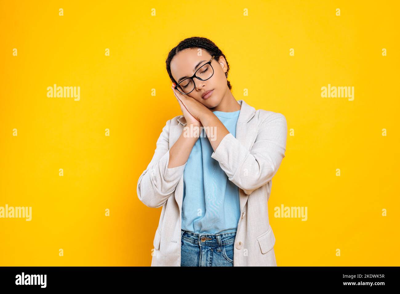 Femme d'affaires fatiguée et surtraitée, portant des lunettes et une veste, montre un geste de sommeil, veut dormir, met sa tête dans ses paumes, ferme ses yeux, se tient sur un fond orange isolé Banque D'Images