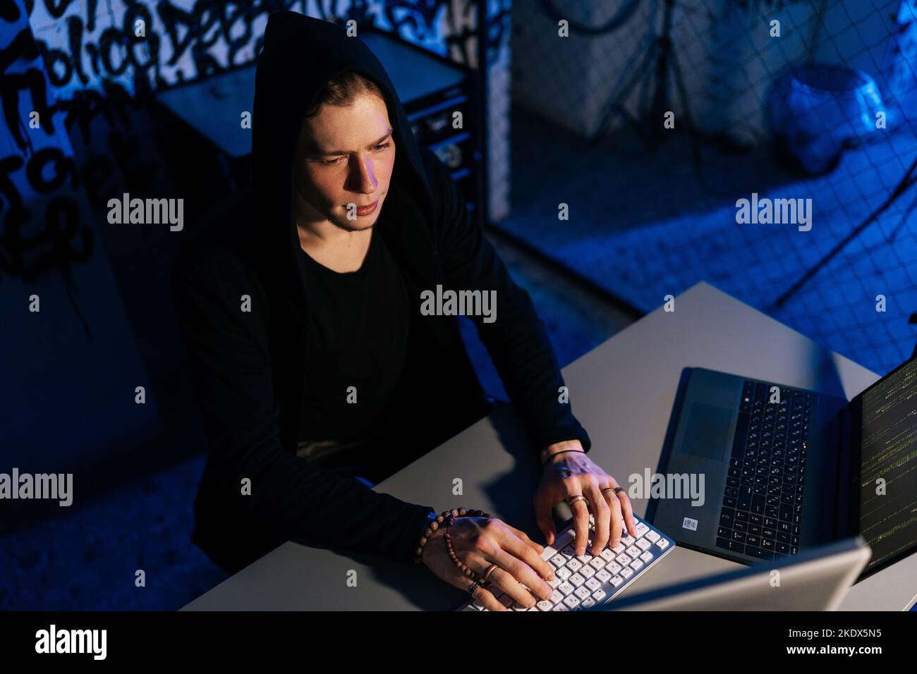 Vue latérale à grand angle d'un pirate dangereux portant un code de frappe à capuchon sur un clavier sans fil, travaillant tard dans la nuit et contournant la cyber-sécurité. Banque D'Images