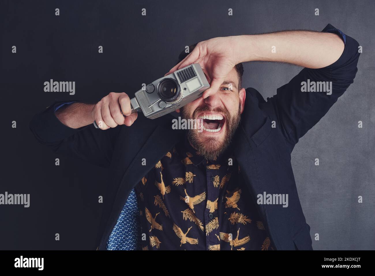 Il a un enthousiasme spécial pour les caméras de cinéma. Un jeune homme tendance avec un appareil photo vintage posant sur un fond sombre. Banque D'Images