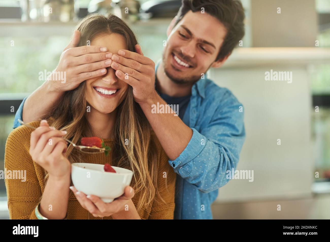 Je me demande qui ça pourrait être... un jeune homme affectueux qui couvre les yeux de ses amies pendant qu'elle mange le petit déjeuner dans leur cuisine. Banque D'Images