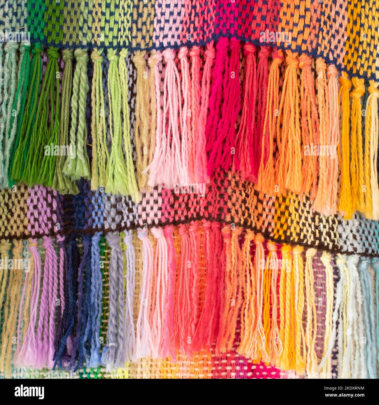 Arrière-plan de tapis multicolore tissé sur le métier à tisser avec des fils noués accrochés sur des cordes dans l'atelier Banque D'Images
