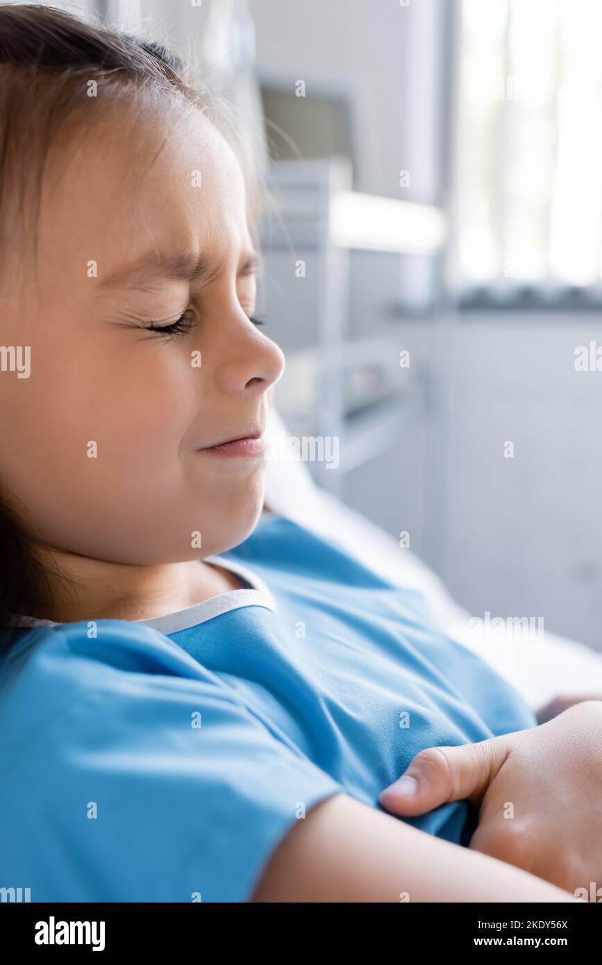 Enfant mécontent et malade dans la robe de patient couché sur le lit dans la clinique, image de stock Banque D'Images