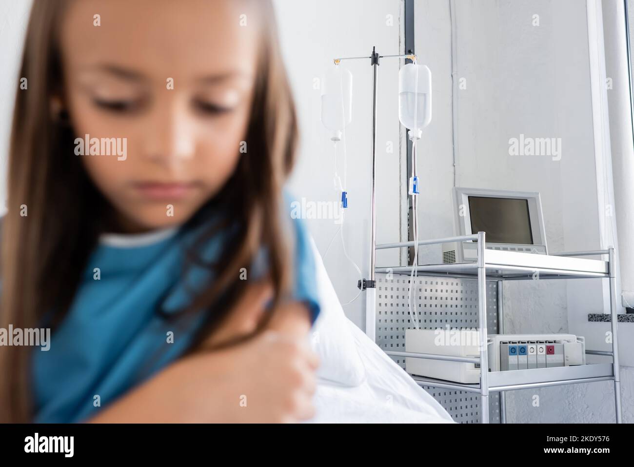 Traitement intraveineux sur le stand près de l'enfant flou dans la robe de patient dans la clinique, image de stock Banque D'Images