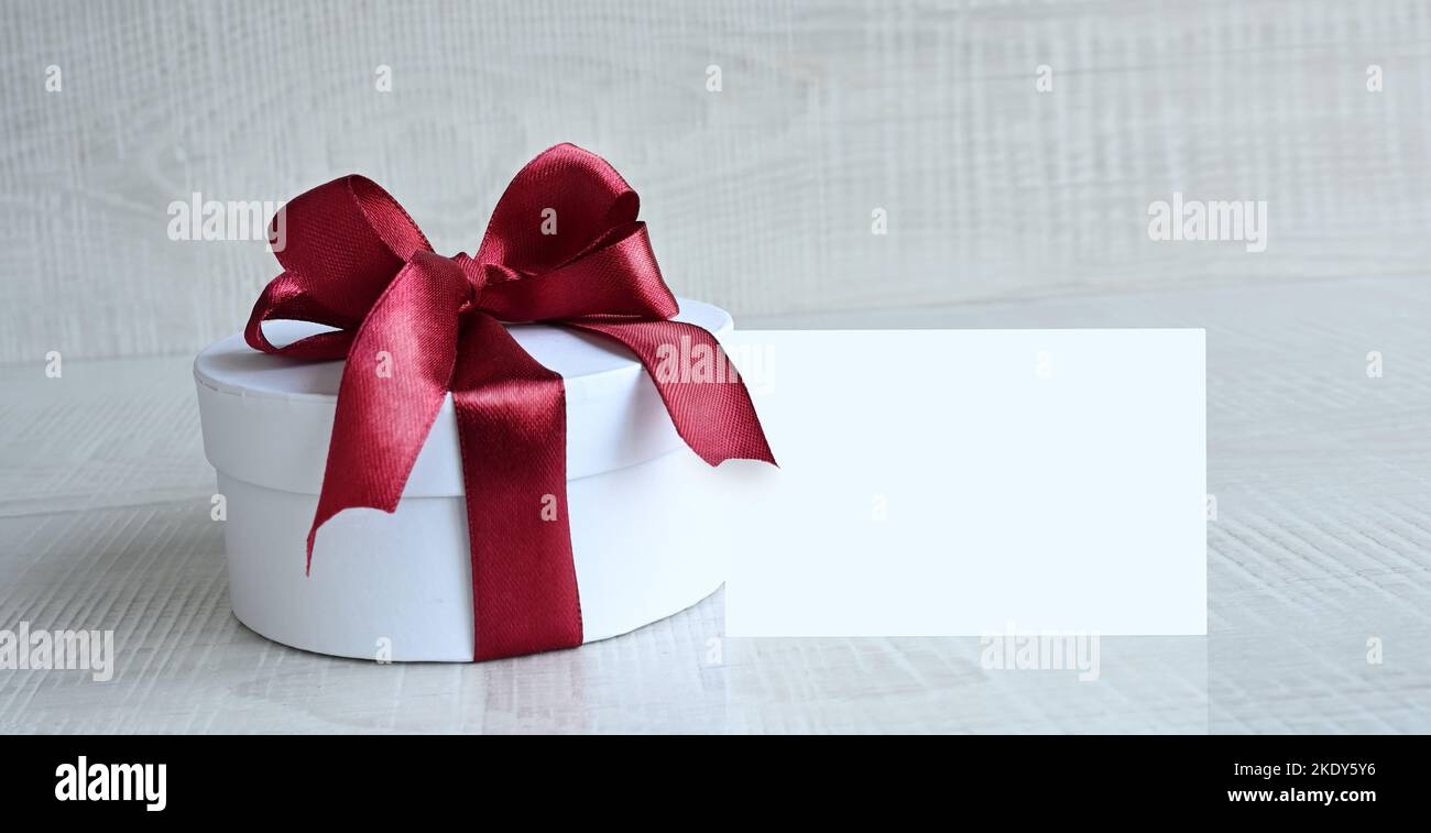Boîte cadeau ronde avec ruban rouge et noeud sur fond gris. Banque D'Images