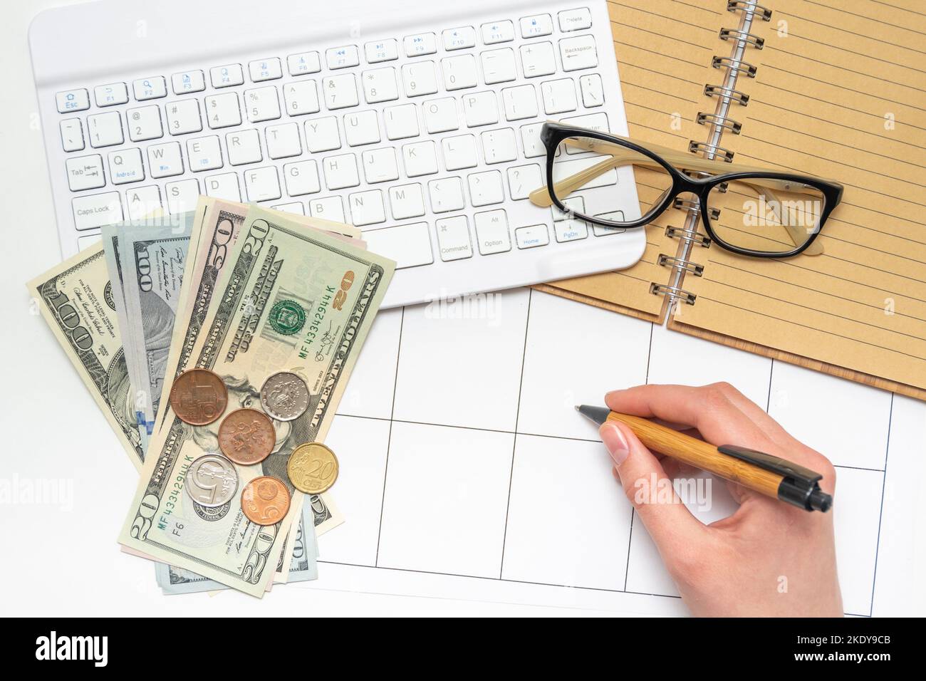 Une main écrivant un rappel dans l'organisateur sur le lieu de travail avec clavier d'argent lunettes bloc-notes. Lieu de travail d'un comptable, financier. Un accord commercial Banque D'Images