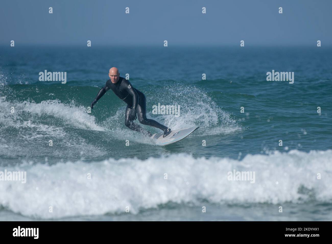 Un surfeur mâle mature qui fait une vague à Fistral, à Newquay, en Cornouailles, au Royaume-Uni. Banque D'Images