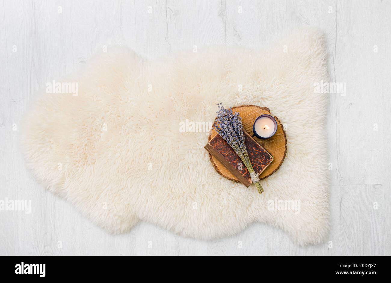Flat Lay vue de blanc chaud et confortable entier véritable tapis décoratif en peau de mouton sur plancher en bois blanc, sur le dessus est livre, fleurs et bougie. Copier l'espace. Banque D'Images