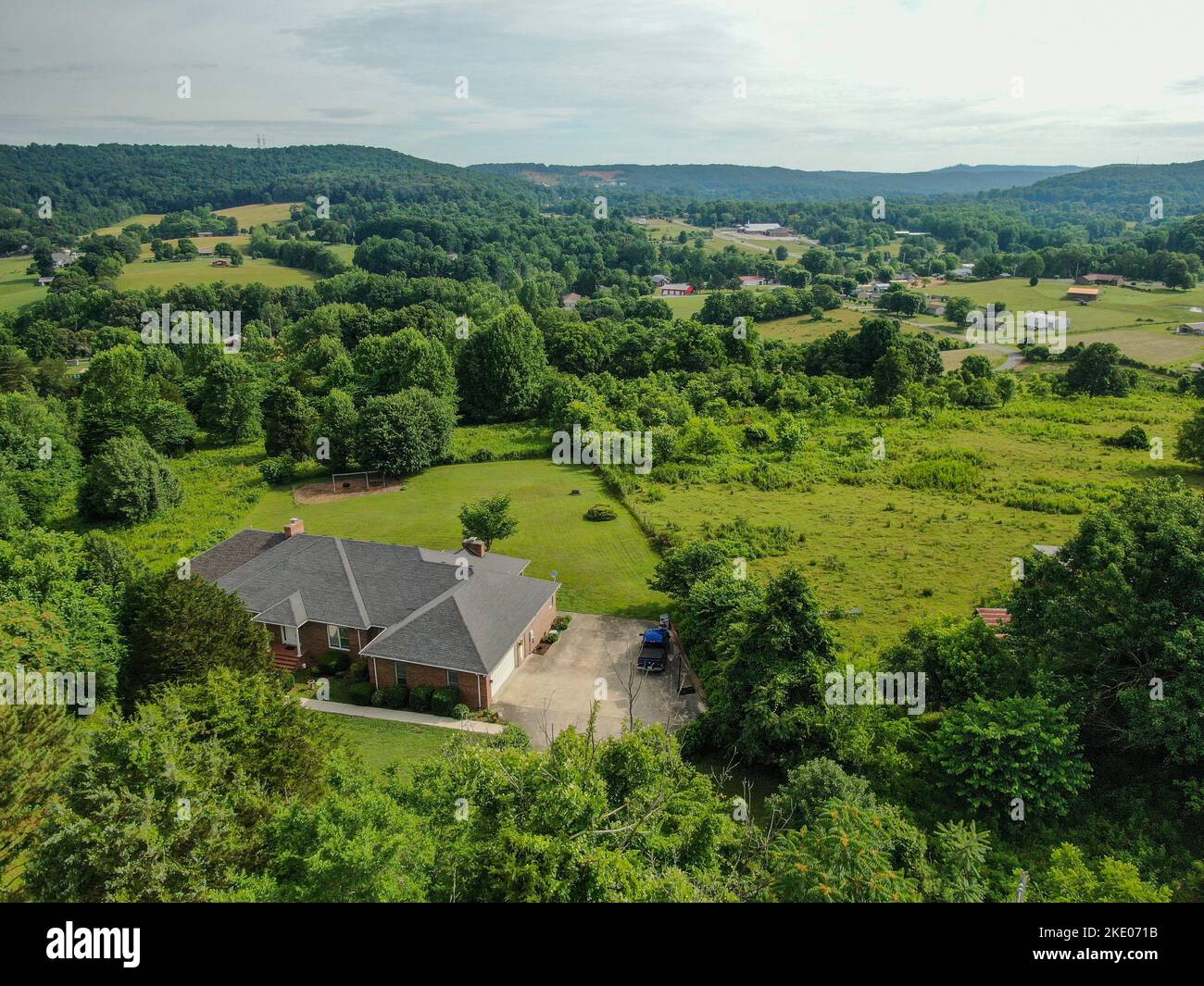 Une vue aérienne d'une maison sur un pré vert à Cookeville, Tennessee, entouré d'arbres, de champs agricoles, et d'une montagne boisée en arrière-plan Banque D'Images