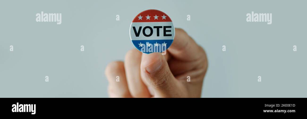 Un jeune homme a un badge de vote pour l'élection des États-Unis dans sa main, sur fond blanc, dans un format panoramique à utiliser comme bannière web Banque D'Images