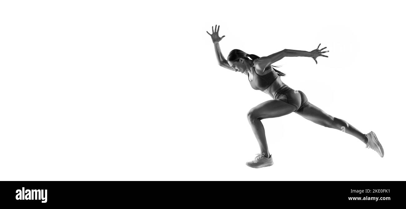 Énergie. Portrait noir et blanc de l'athlète professionnelle féminine, coureur, jogger en action isolé sur fond blanc. Monochrome. Sport, beauté Banque D'Images