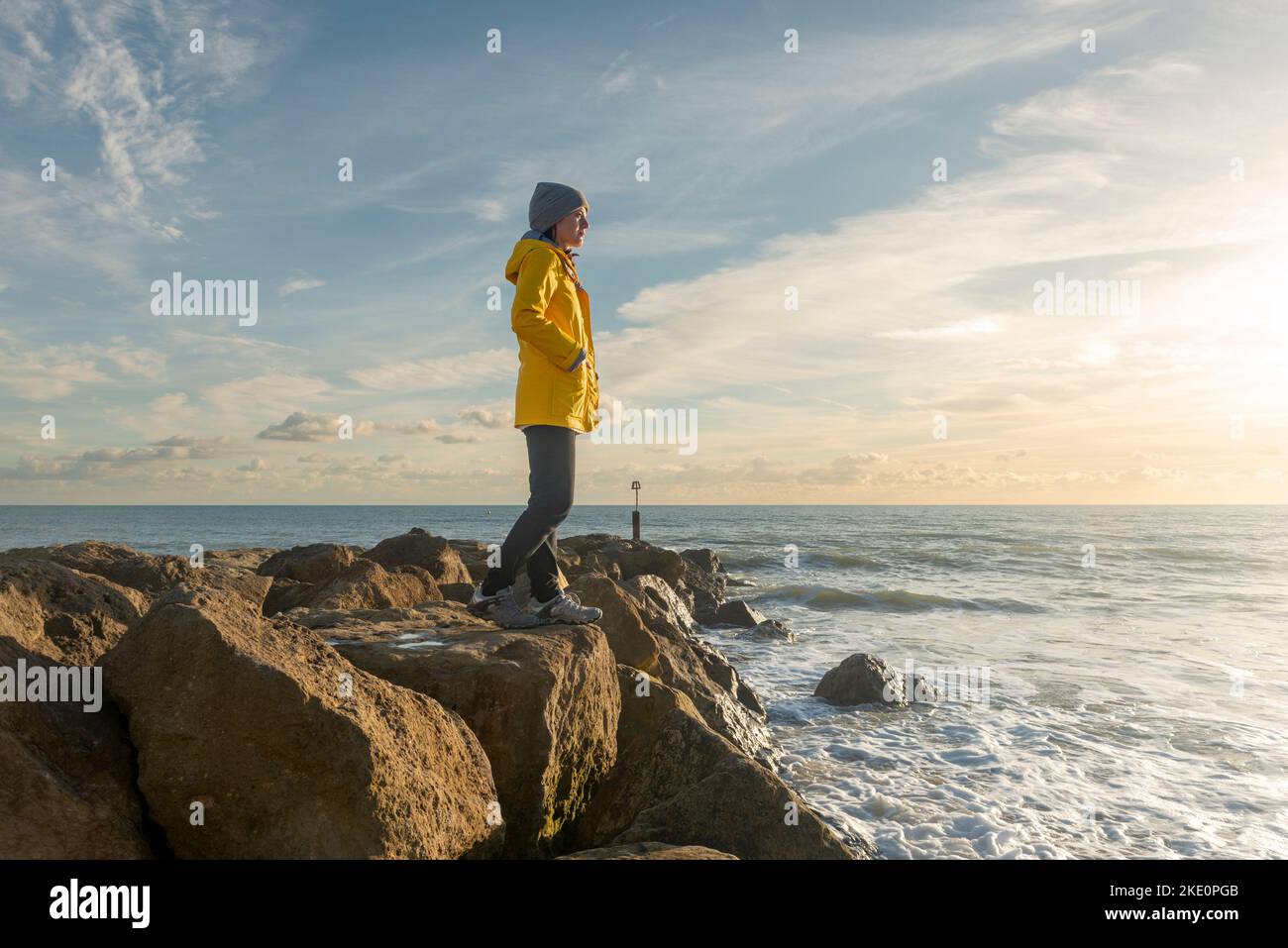 Femme debout sur des rochers regardant l'océan, manteau jaune. Banque D'Images Femme debout sur des rochers regardant l'océan, manteau jaune. Banque D'Images