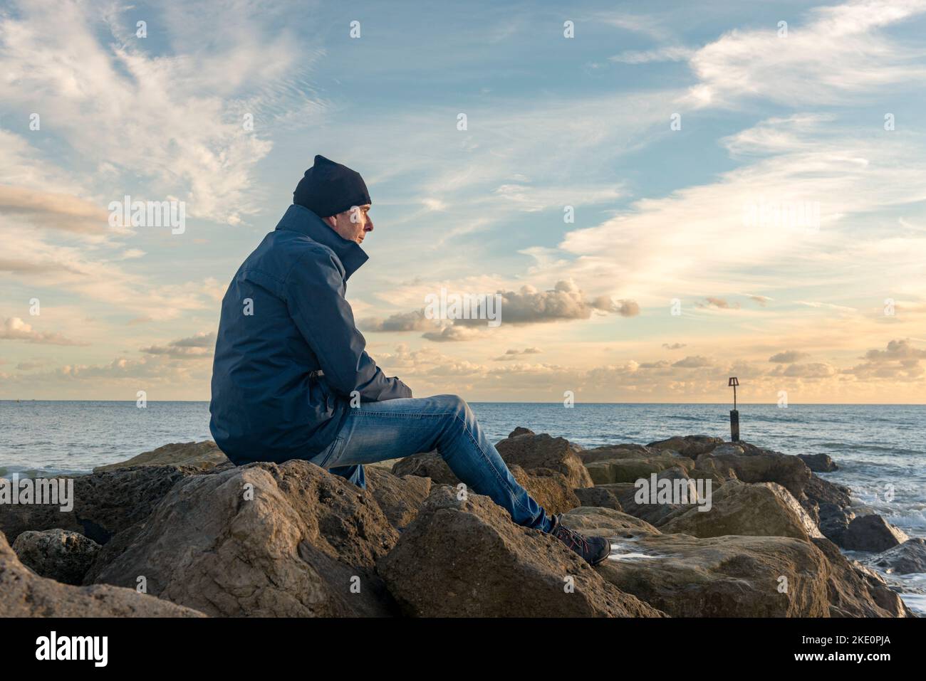 Homme assis seul sur des rochers regardant la mer. Banque D'Images