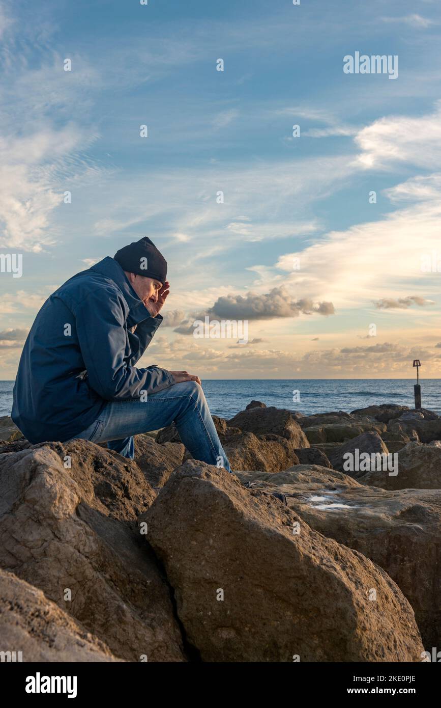 homme assis sur des rochers au bord de la mer avec sa tête dans ses mains, ses émotions, concept de santé mentale Banque D'Images