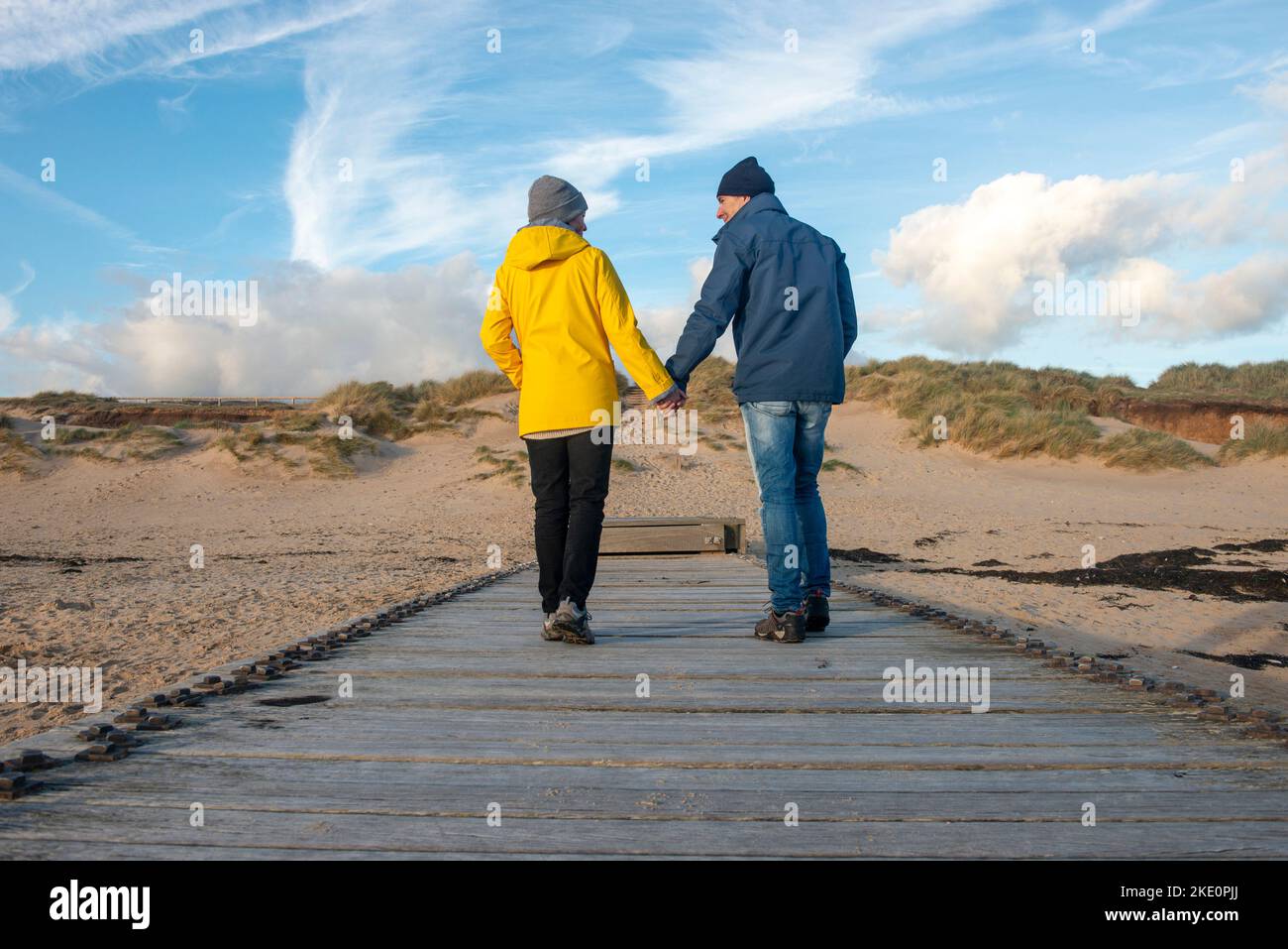 Couple marchant le long d'une promenade sur une plage tenant les mains. Banque D'Images