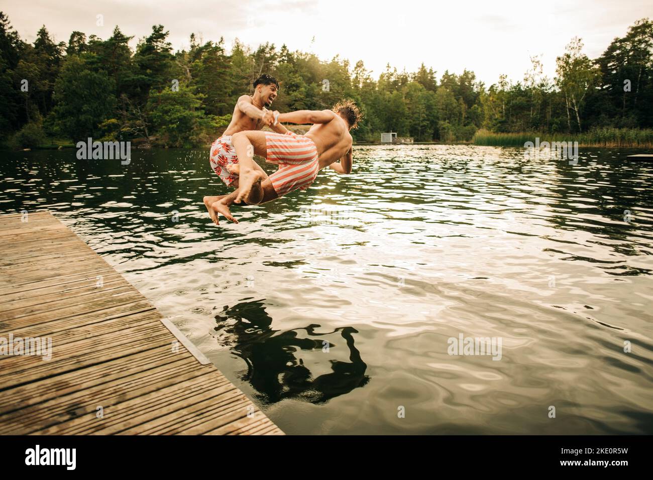 Amis masculins joueurs sautant ensemble dans le lac pendant les vacances Banque D'Images