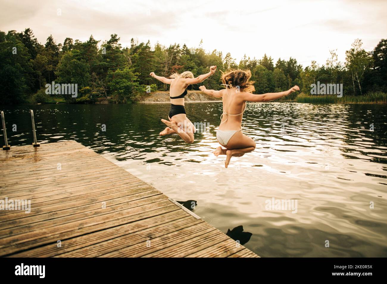 Les amies portant le maillot sautant dans le lac avec les bras étirés pendant les vacances Banque D'Images