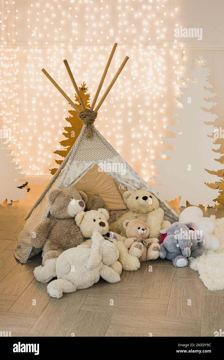 Zone de photo pour enfants dans le studio de photo de Noël - wigwam avec ours en peluche sur fond de silhouettes de sapins et de guirlandes. Banque D'Images