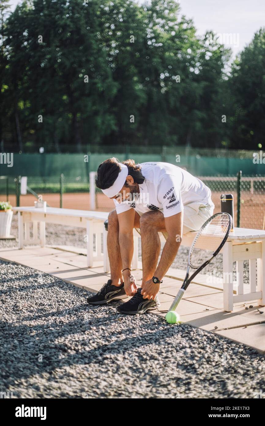 Homme attachant la dentelle des chaussures en étant assis sur le banc au court de tennis Banque D'Images