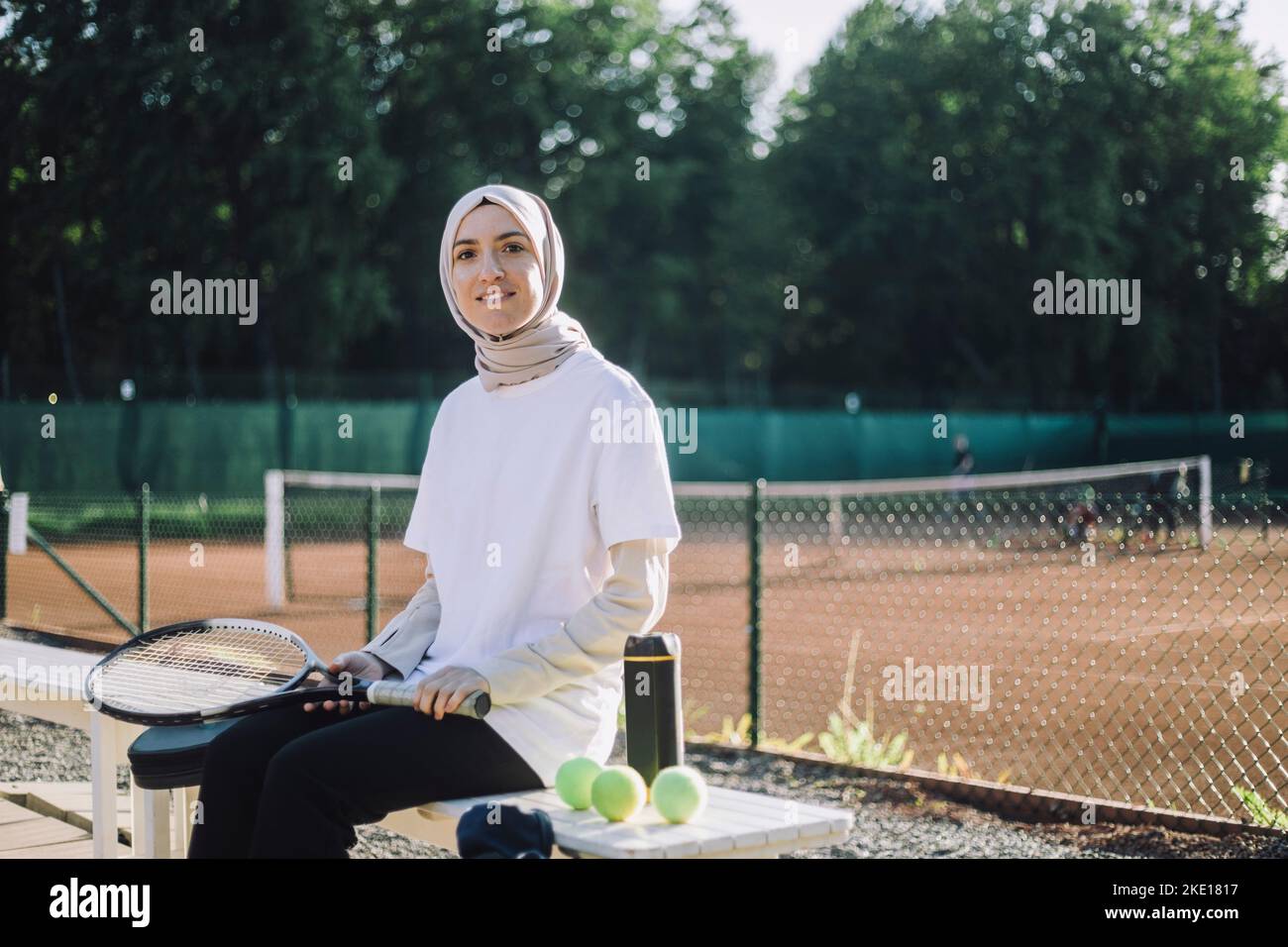 Portrait d'une femme portant un foulard tenant une raquette de tennis assis sur un banc sur un terrain de sport Banque D'Images