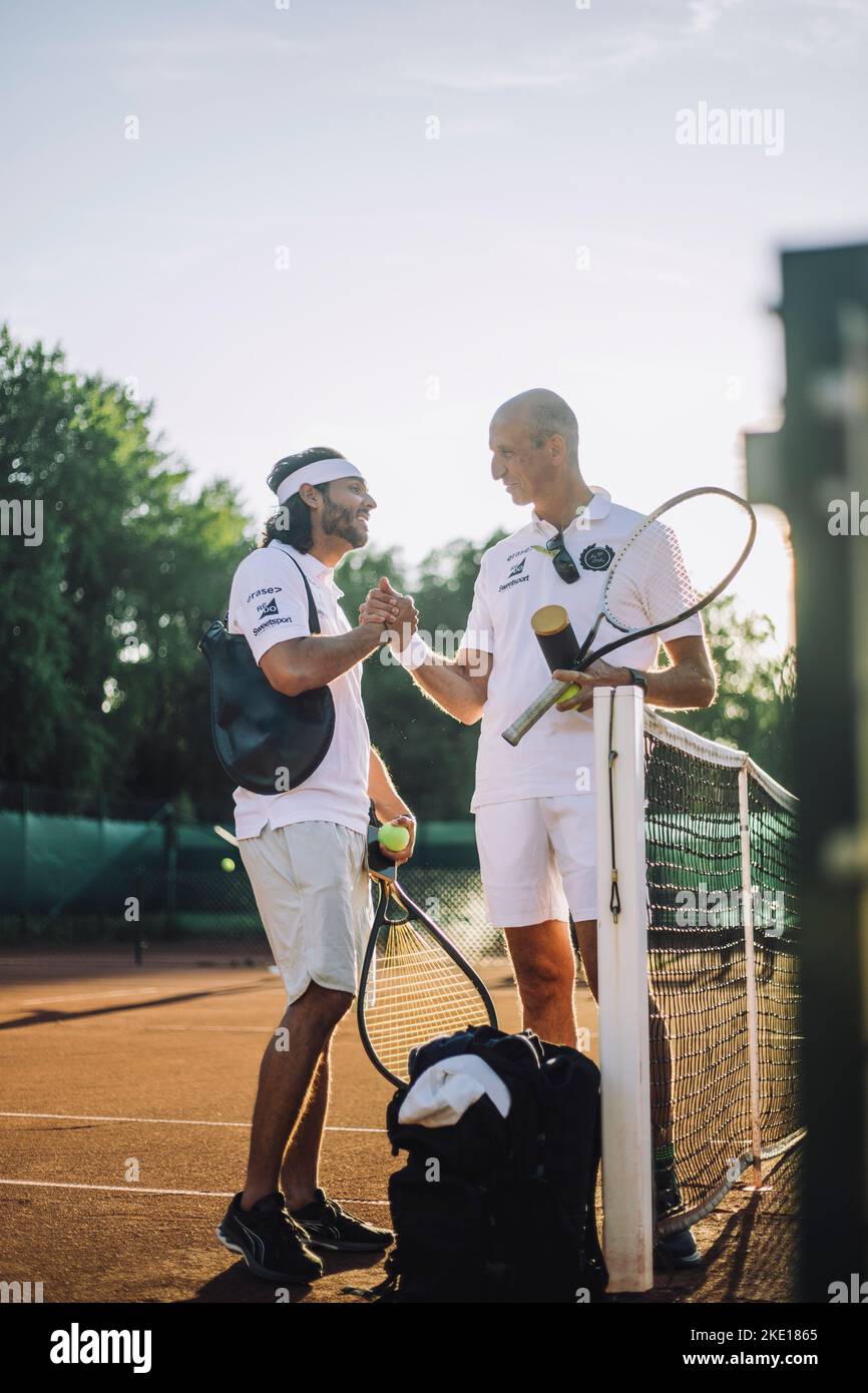 Hommes échangeant poignée de main tenant une raquette de tennis tout en se tenant sur un terrain de sport Banque D'Images