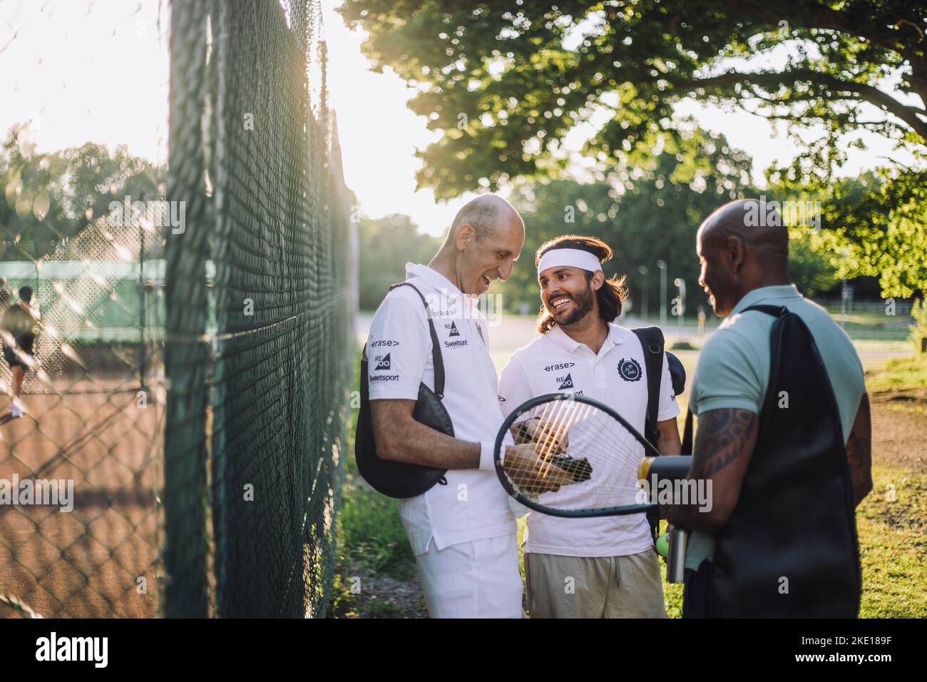 Des amis masculins heureux parlent les uns aux autres tout en se tenant près de la clôture Banque D'Images