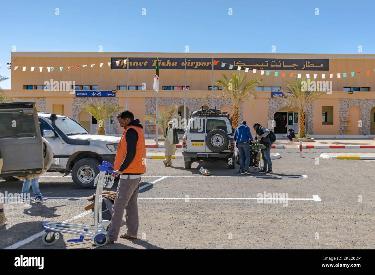 Aéroport de Tiska Djanet Inedbirene, personnes se préparant dans le stationnement, véhicules 4X4 garés portes ouvertes, ouvrier local et tuareg homme posant. Banque D'Images