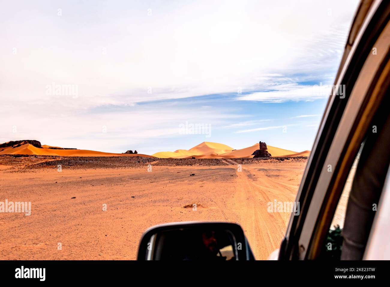 Vue du passager arrière à l'extérieur de la fenêtre d'une voiture en mouvement dans le désert du Sahara. Offroad reg, dunes de sable, mesa rocheuse et un ciel couvert de bleu à Tassili n'Ajjer. Banque D'Images