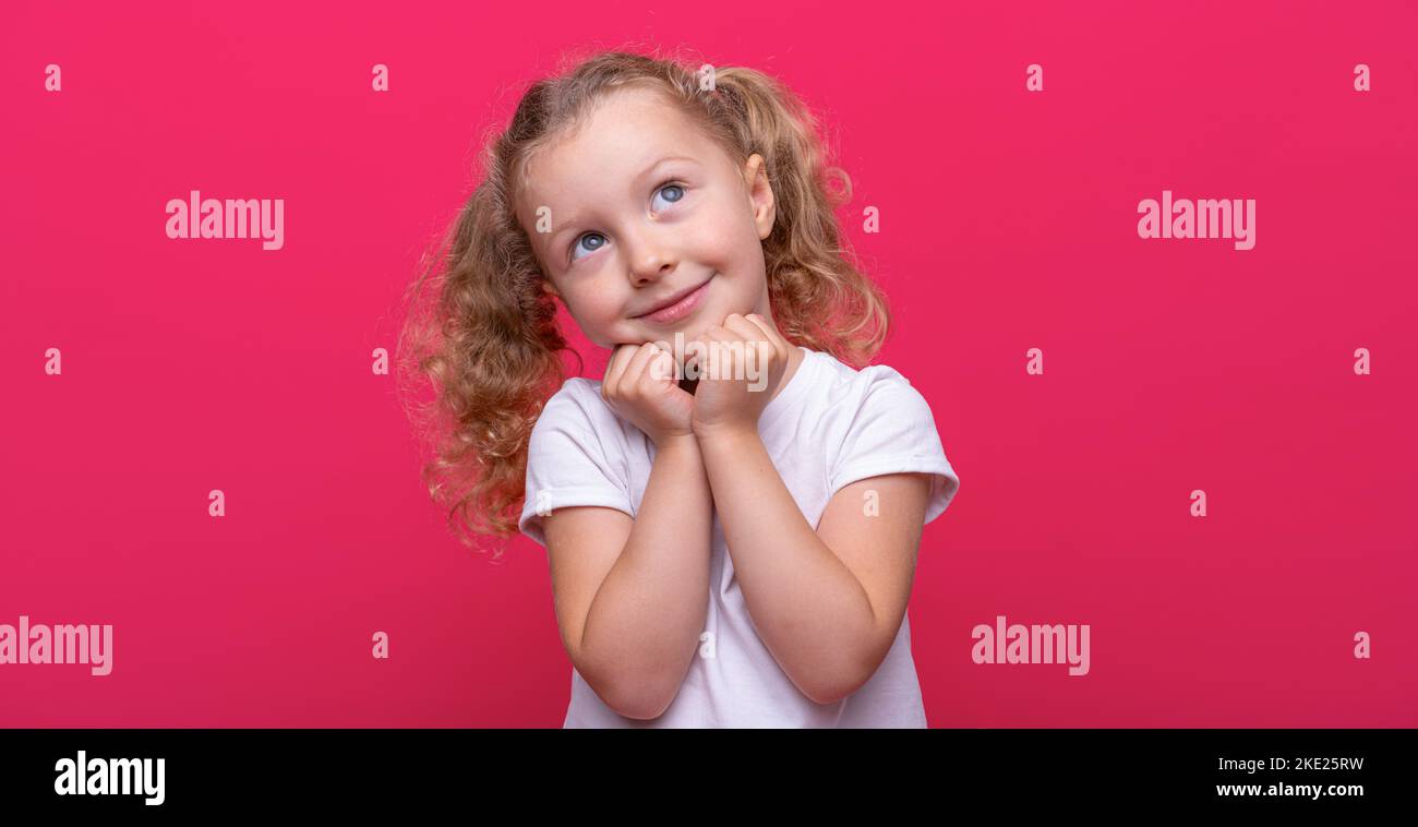 Rêve d'une petite fille dans un t-shirt blanc sur fond rose. Banque D'Images