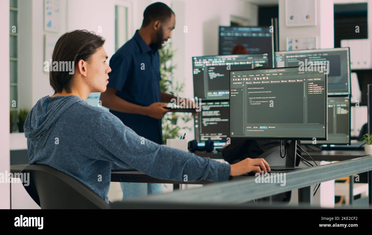 Développeur de logiciels saisissant le code de l'application d'apprentissage sur l'ordinateur, assis au bureau du Big Data. Programme de cloud qui travaille avec le script de base de données html dans une agence de cybersécurité. Prise de vue à main levée. Banque D'Images