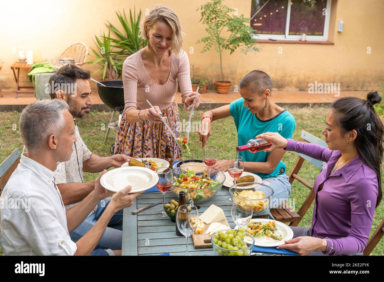 La femme sert la nourriture dans le patio de la maison. Des amis heureux qui rient autour de la table à l'extérieur. Banque D'Images