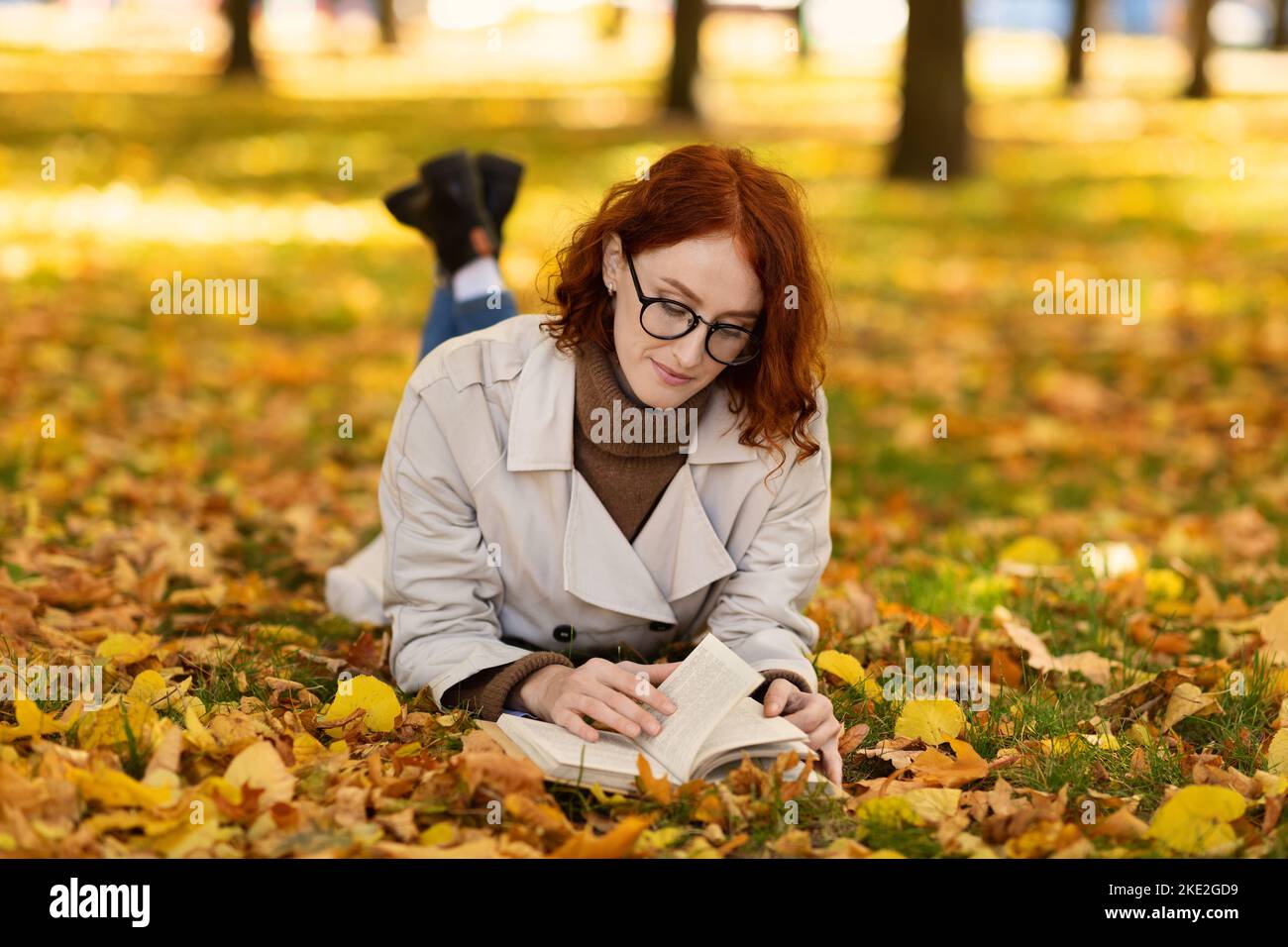 Femme millénaire caucasienne sérieuse concentrée avec des cheveux rouges en imperméable et des lunettes au sol Banque D'Images