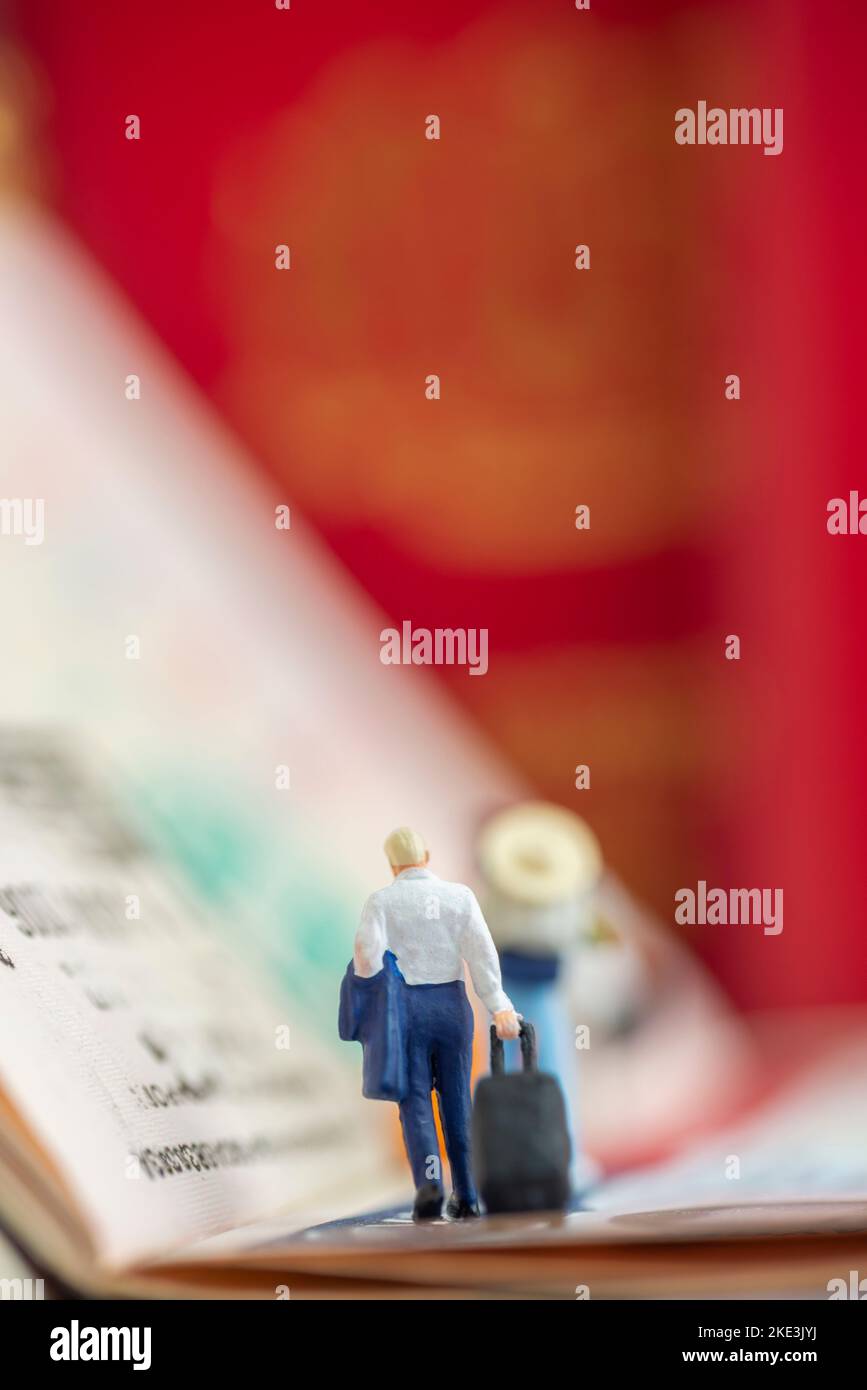 Création d'un studio de concept de jouets miniatures - un homme d'affaires expatrié tirant un bagage arrive ou part avec des timbres de passeport de visa comme arrière-plan. Banque D'Images