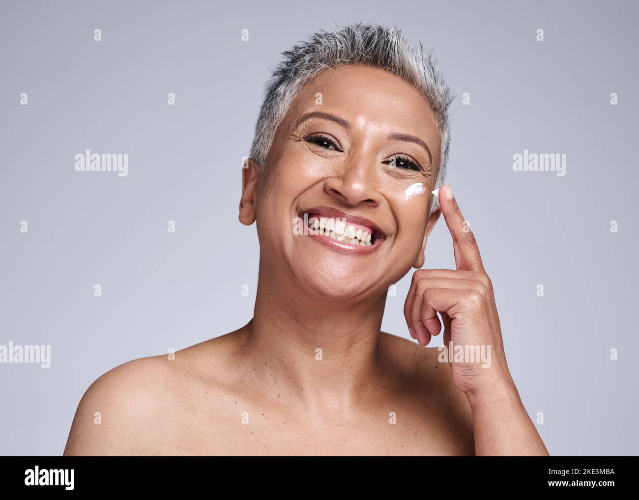 Soin de la peau, crème faciale et femme noire sénior isolée sur fond gris en studio pour spa. La beauté, le bien-être et le portrait de la vieille femme appliquent la lotion Banque D'Images