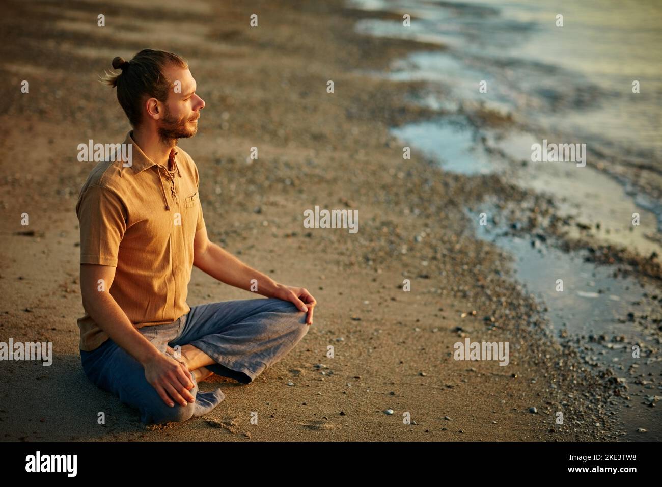 La nature peut transformer le chaos en calme. Un homme assis dans la position de lotus pendant sa routine de yoga à la plage. Banque D'Images
