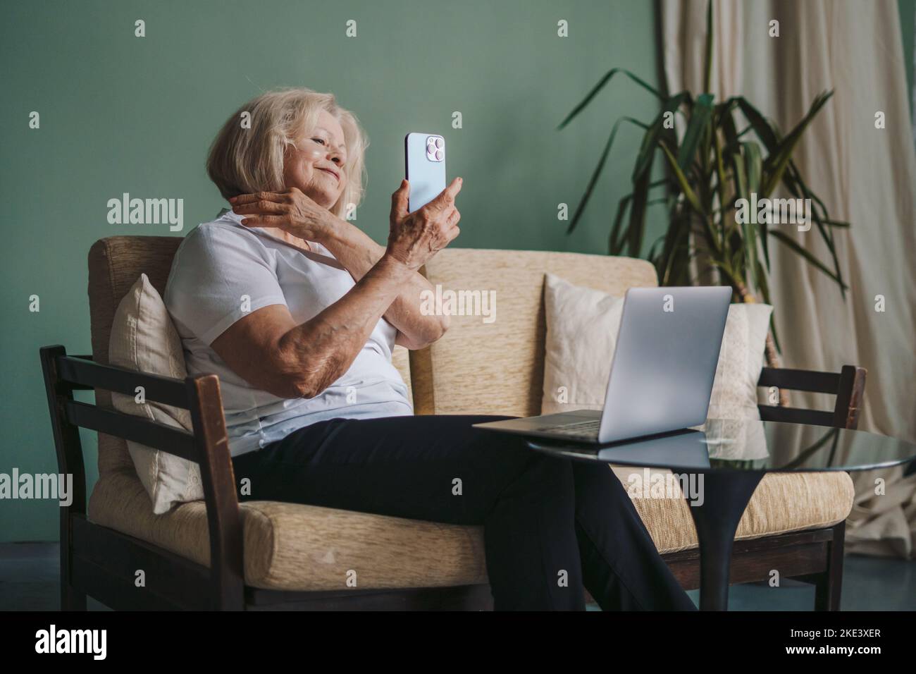 Femme âgée, tenant un smartphone à la main, assise à la maison sur un canapé. Achats en ligne, technologie Internet sur téléphone portable. Banque D'Images