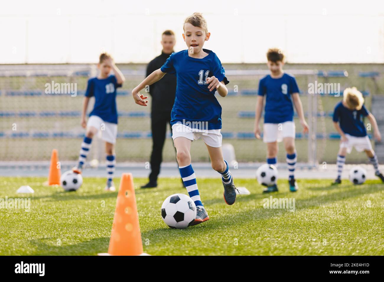 Jeunes footballeurs européens. Happy Kids sur l'entraînement d'entraînement de football. Garçons de football en entraînement avec un jeune entraîneur d'école Banque D'Images