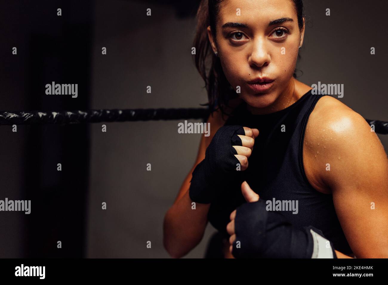 Femme sportive debout dans un anneau de boxe avec les mains enveloppées avant un combat. Boxeur féminin ayant une séance d'entraînement dans un gymnase de boxe. Banque D'Images Femme sportive debout dans un anneau de boxe avec les mains enveloppées avant un combat. Boxeur féminin ayant une séance d'entraînement dans un gymnase de boxe. Banque D'Images