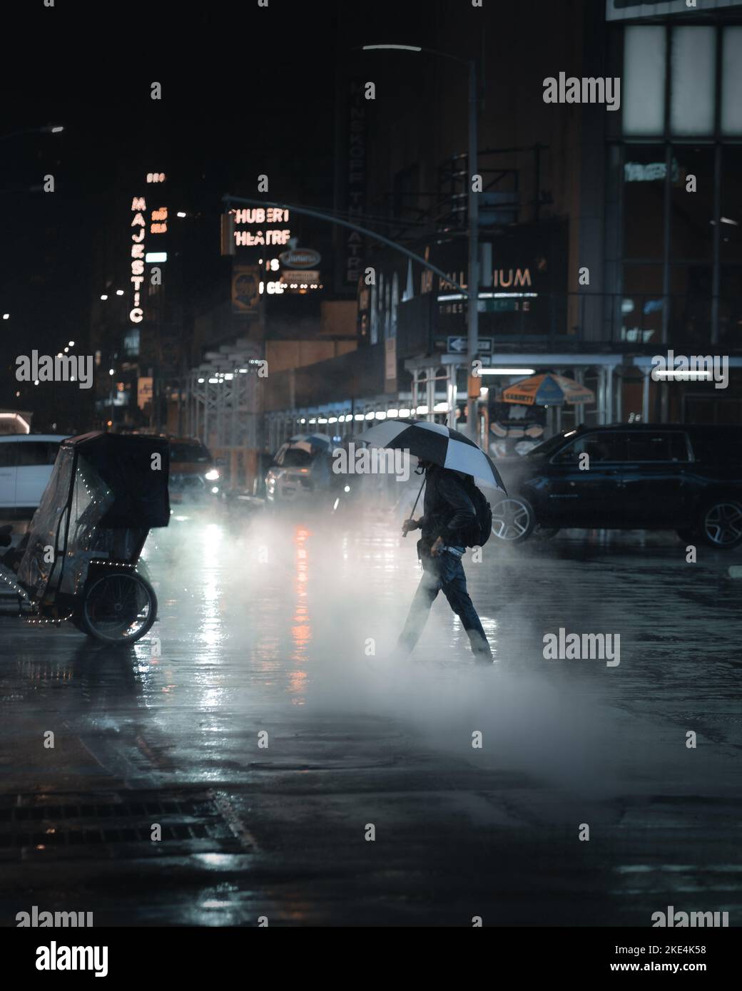 Un homme avec un parapluie traversant une rue avec beaucoup de vapeur pendant une nuit de pluie sur Times Square à New york Banque D'Images