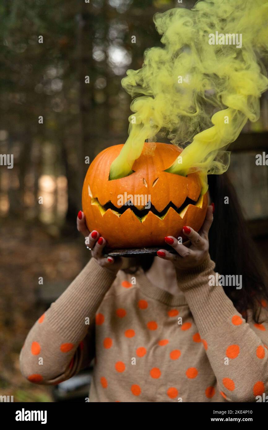 Jeune belle femme tenant la citrouille d'halloween avec la fumée jaune Banque D'Images