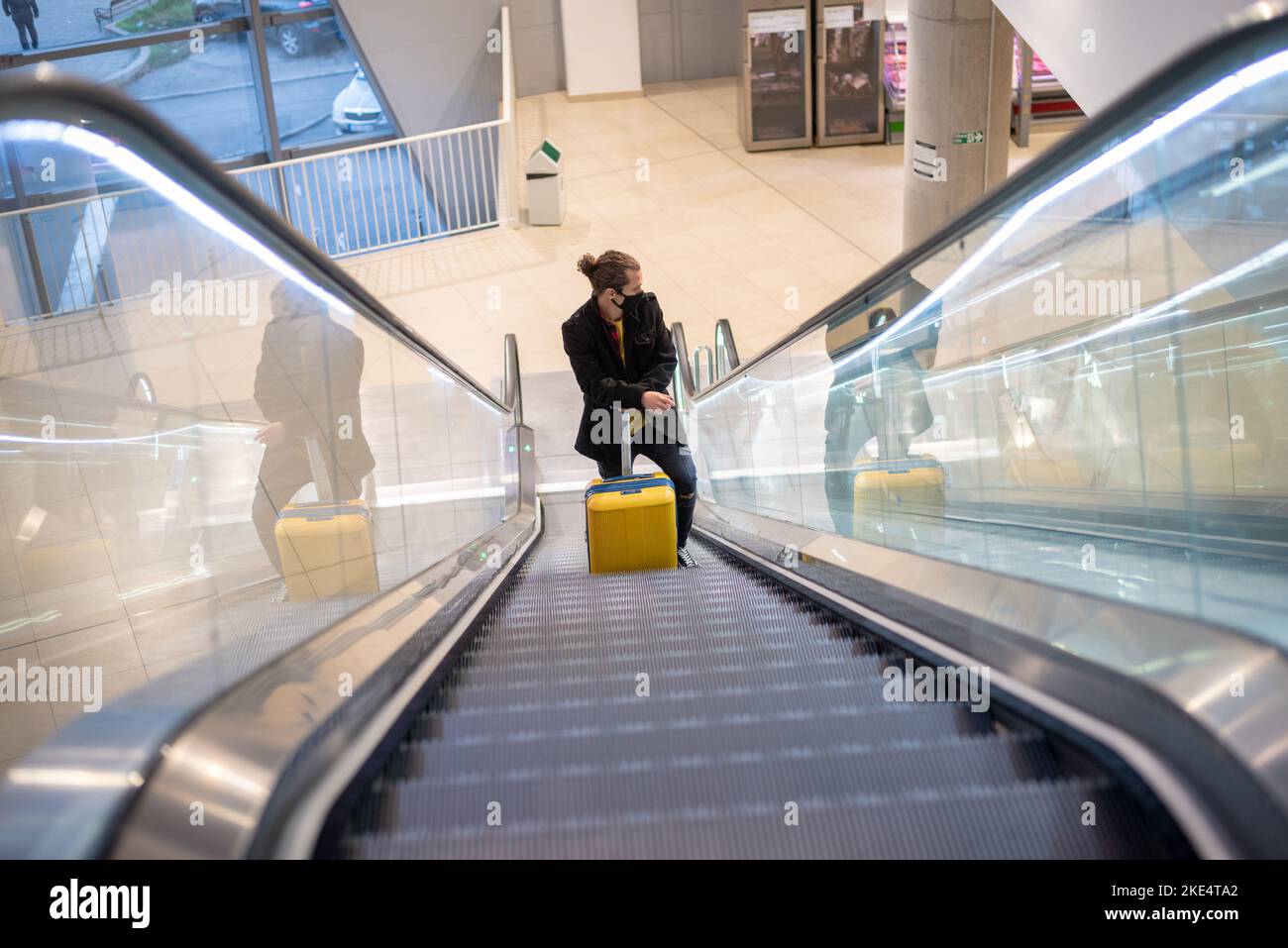 Homme à l'aéroport avec une valise à roulettes sur l'escalier roulant Banque D'Images