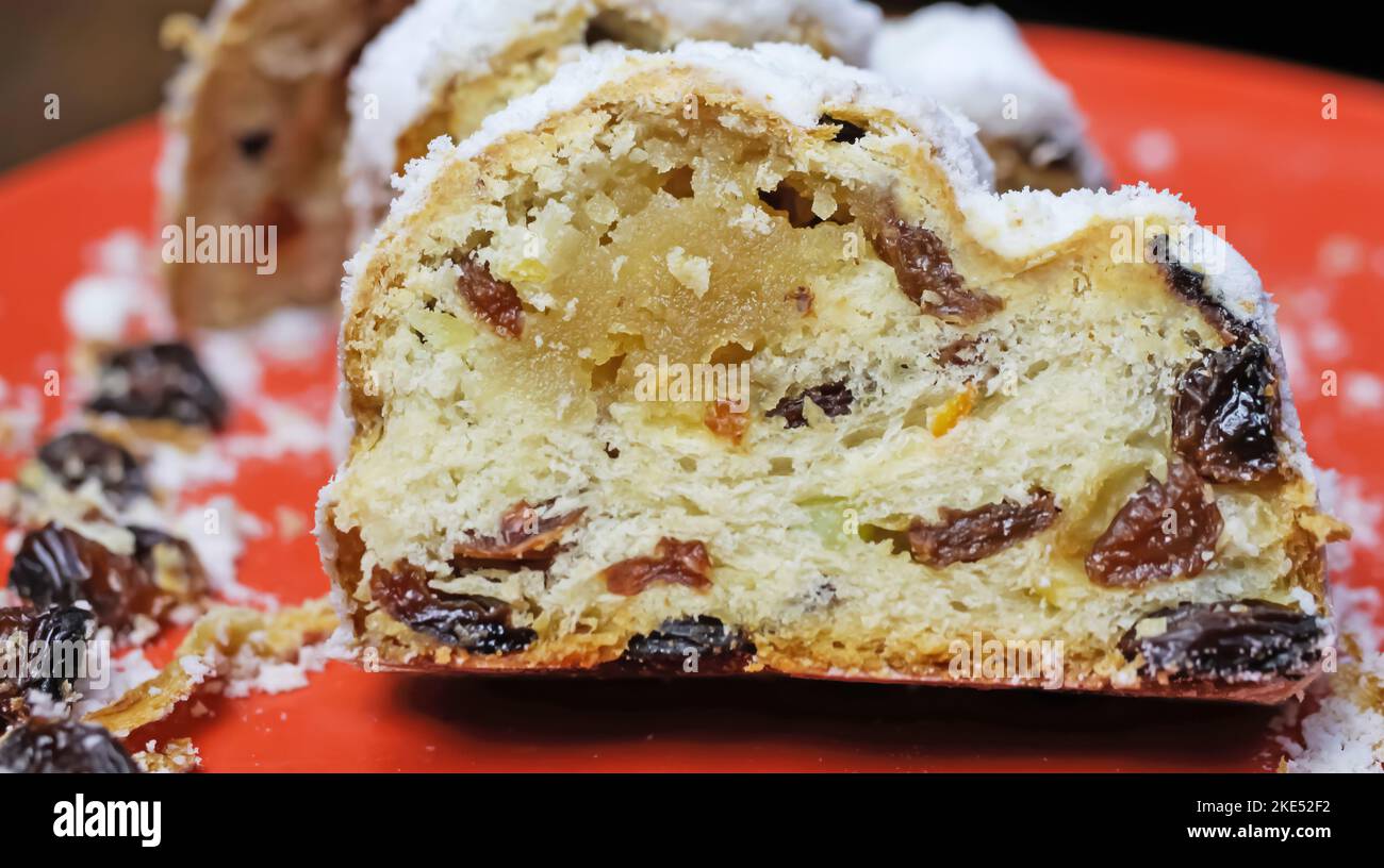 Gros plan de christstollen tranché isolé avec des raisins secs, du sucre blanc en poudre et du massepain sur la plaque rouge Banque D'Images